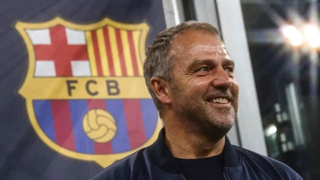 Hansi Flick smiling in front of the FC Barcelona club crest