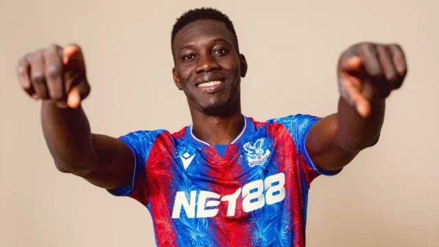 Ismaila Sarr wearing a blue and red Crystal Palace football kit, pointing forward with both hands.
