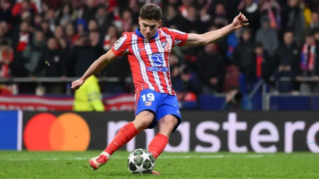 Julian Alvarez wearing the Atletico Madrid home kit kicking a soccer ball during a match