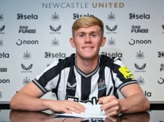 Transferência de David Raum: Explicação do interesse do Manchester United Lewis Hall smiling while signing a contract in a Newcastle United jersey against a club sponsor backdrop.