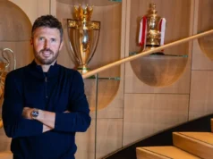 Transferência de Jonathan David: atacante peso do United Juventus Michael Carrick posing with arms crossed in front of gold trophies in a modern wooden interior