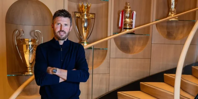 Michael Carrick posing with arms crossed in front of gold trophies in a modern wooden interior