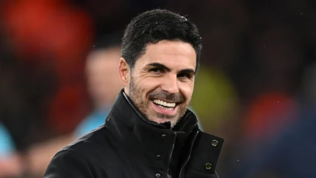 Julián Álvarez Arsenal Move Enters Transfer Picture Portrait of Mikel Arteta smiling, wearing a black jacket against a blurred stadium background.